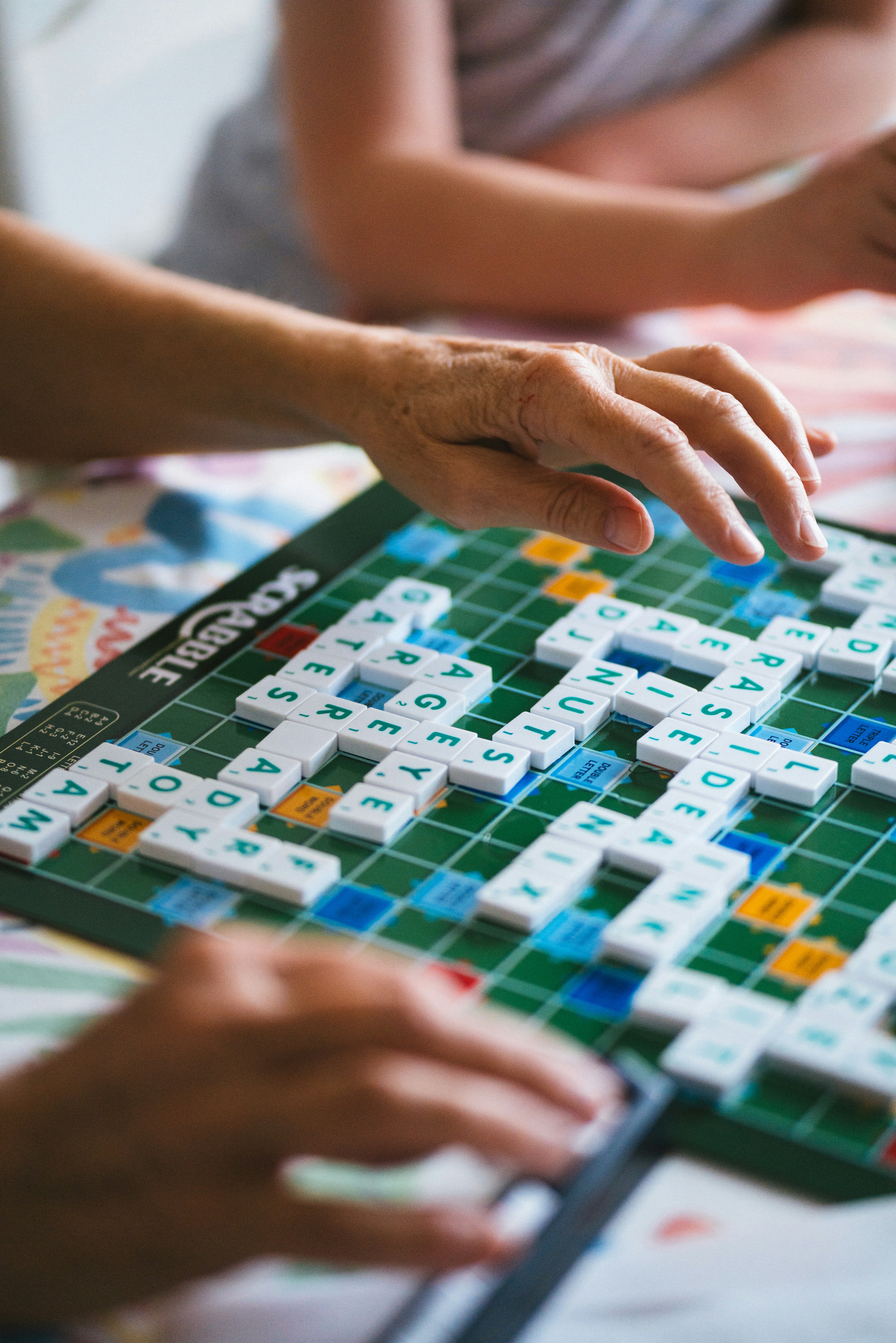 A couple of people playing a game of scrabble. They are mostly offscreen and we only see their hands.